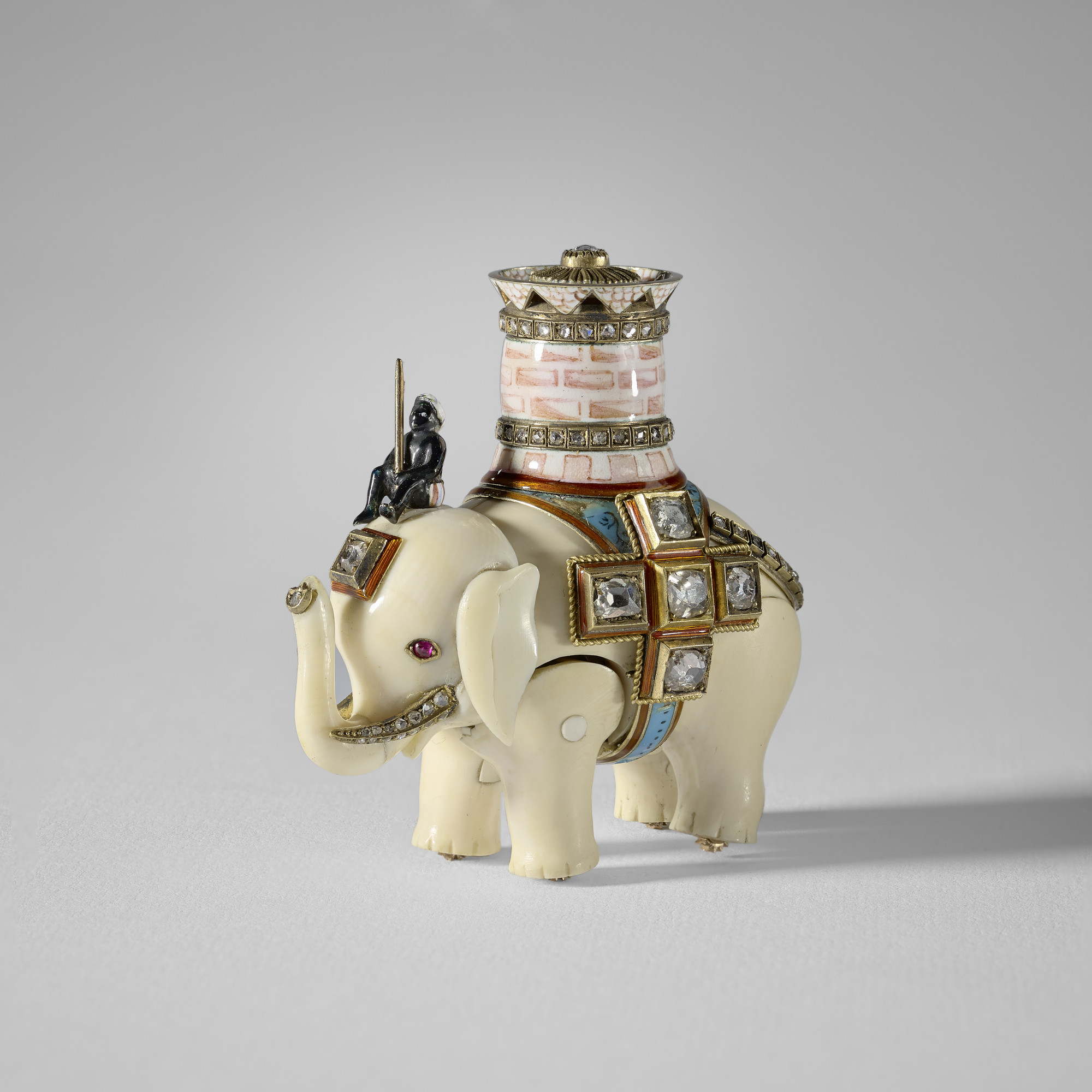 An ivory elephant with separate, jointed body legs&nbsp;and head, ridden by an enamel man sitting on its head&nbsp;and carrying a pink&nbsp;and white enamel castle with two&nbsp; rose cut diamond set bands&nbsp;and a pierced upper rim, the top set with a 