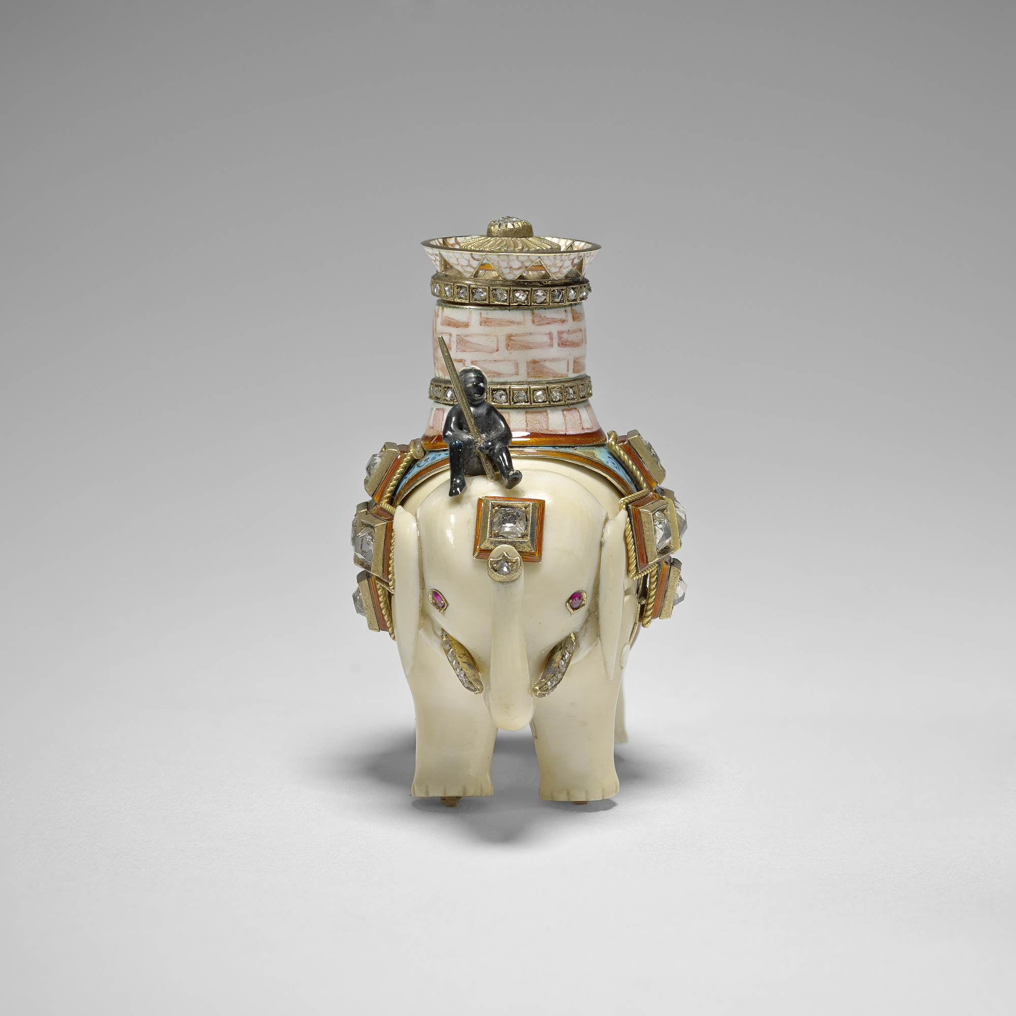 An ivory elephant with separate, jointed body legs&nbsp;and head, ridden by an enamel man sitting on its head&nbsp;and carrying a pink&nbsp;and white enamel castle with two&nbsp; rose cut diamond set bands&nbsp;and a pierced upper rim, the top set with a 