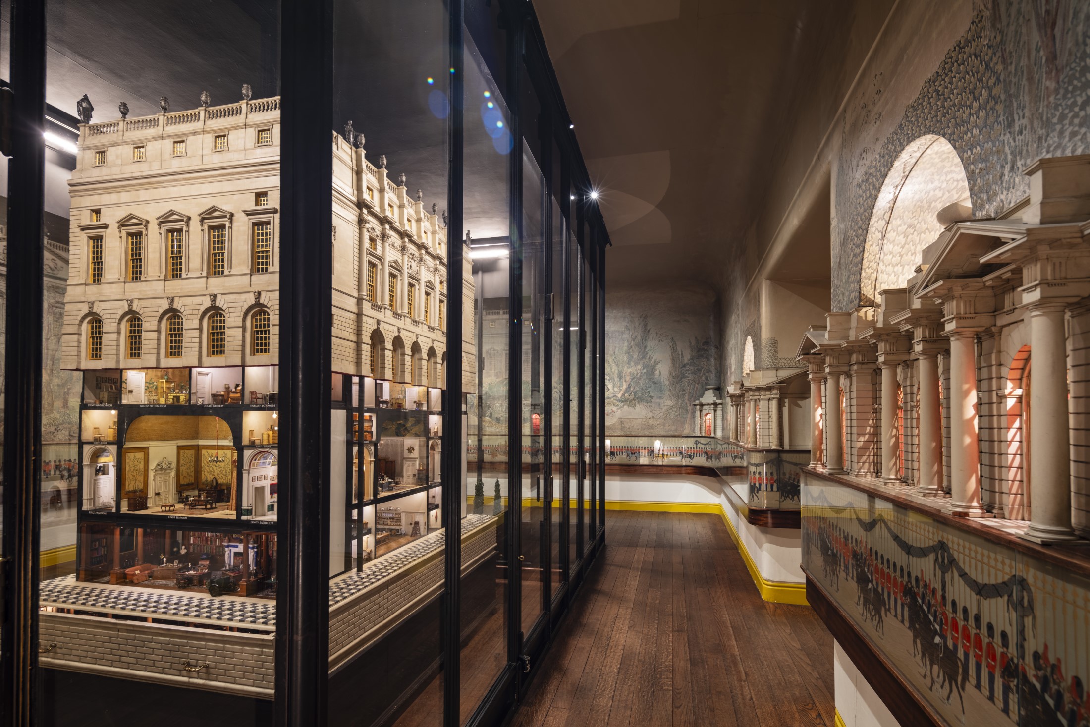 A view of the Dolls' House allowing you to see into the rooms, surrounded by murals showing a wooded park