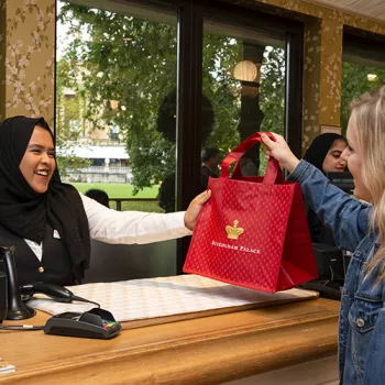 A woman at a cashier desk hands a customer a red bag of her purchases