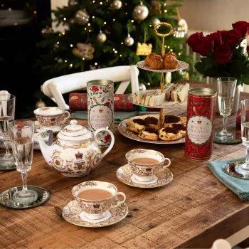 Items from the Royal Collection Trust Christmas suc has tubes of biscuits and crackers, with items from the Victoria & Albert range, including a white teapot and matching tea cups, on a table with wine